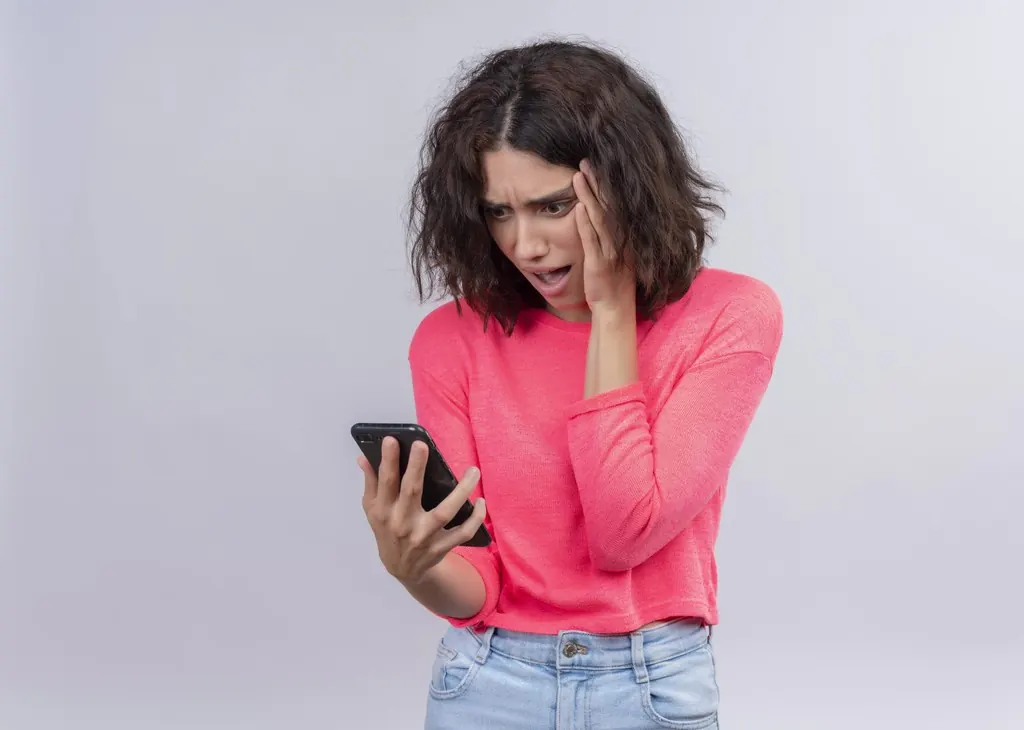 An anxious young woman looking at her phone with her hand on her cheek